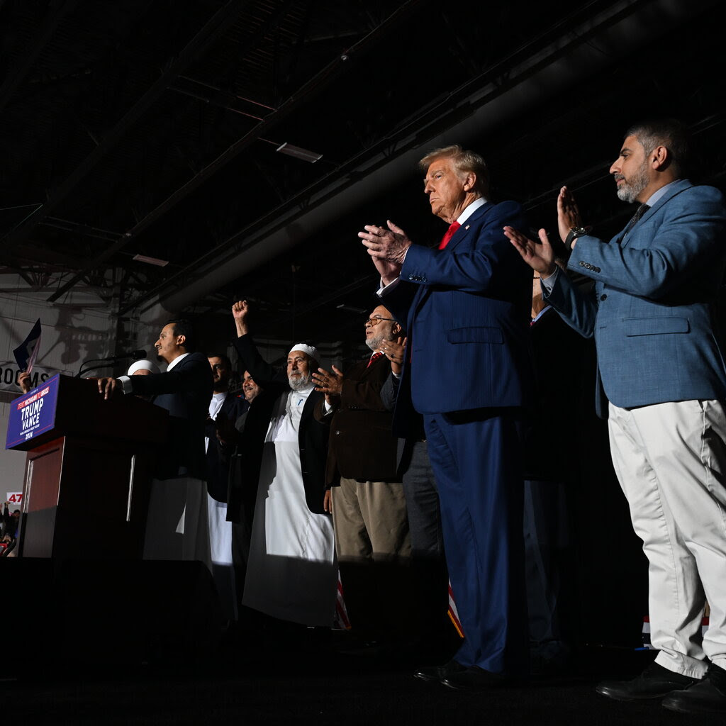 Donald Trump stands and claps on a stage along with several other men.