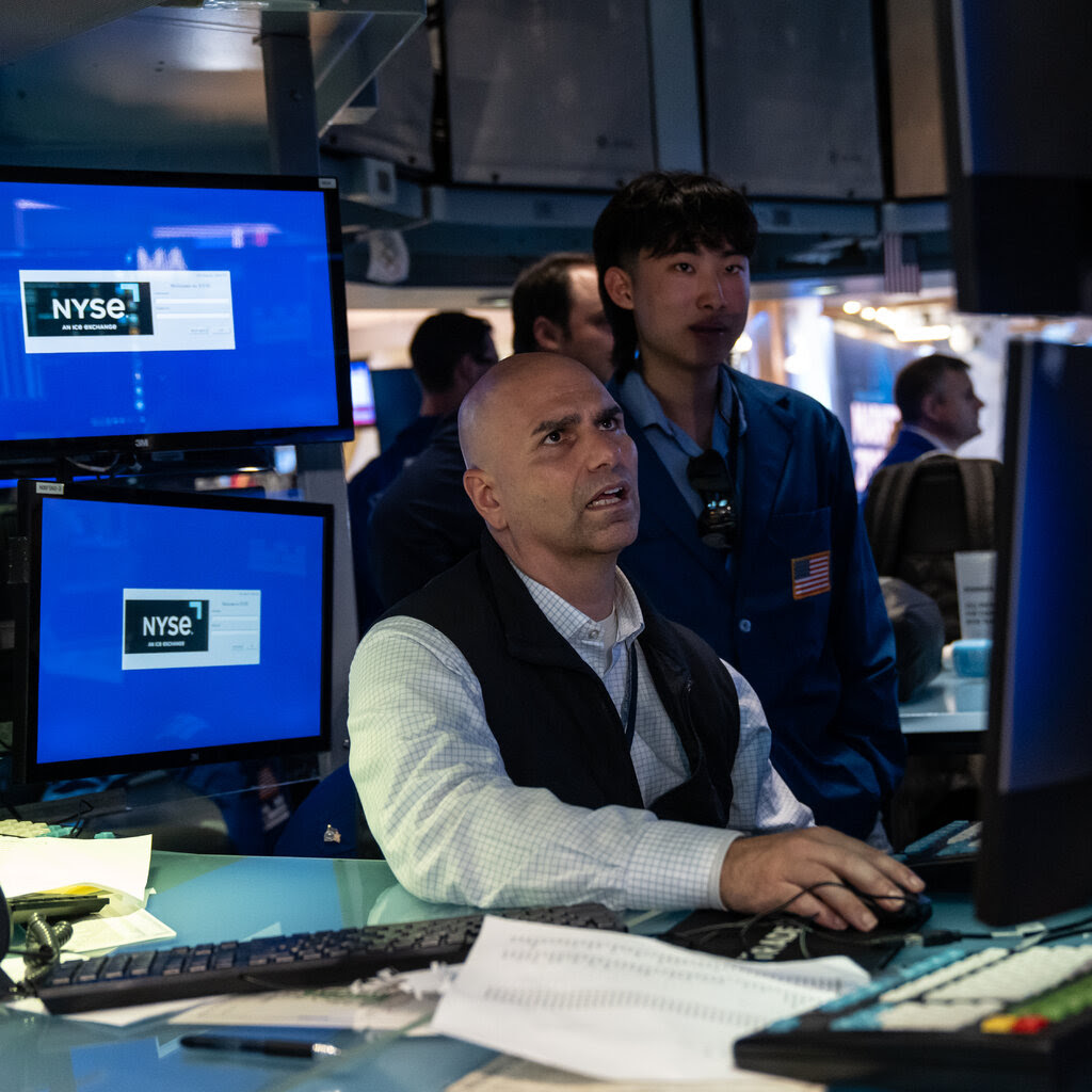 Two people, one standing and one sitting, look at computer screens. Next to them are more computers.