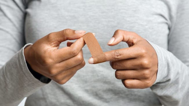 Close-up of person's hands. The person is putting an adhesive bandage on their left index finger.