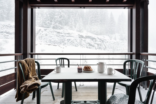 A table with food on it and chairs in front of a windowDescription automatically generated