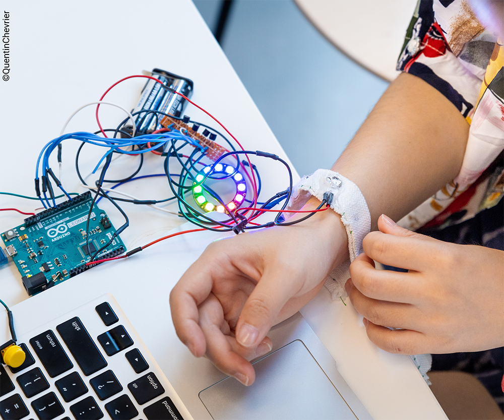 The arm of a young person, attached to a series of glowing wires and a laptop