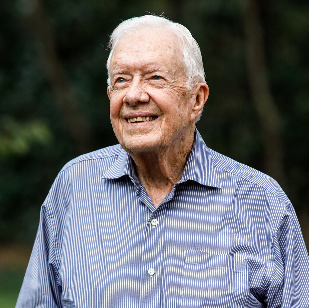 A portrait of Jimmy Carter wearing a blue collared shirt and jeans.