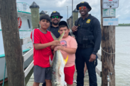 Two NOAA Enforcement Officers and two children with pose holding a crevalle jack on a pier