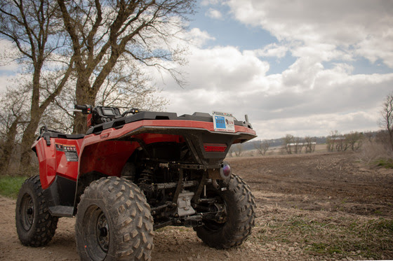 A red ATV is parked a on trail next to a barren crop field. 