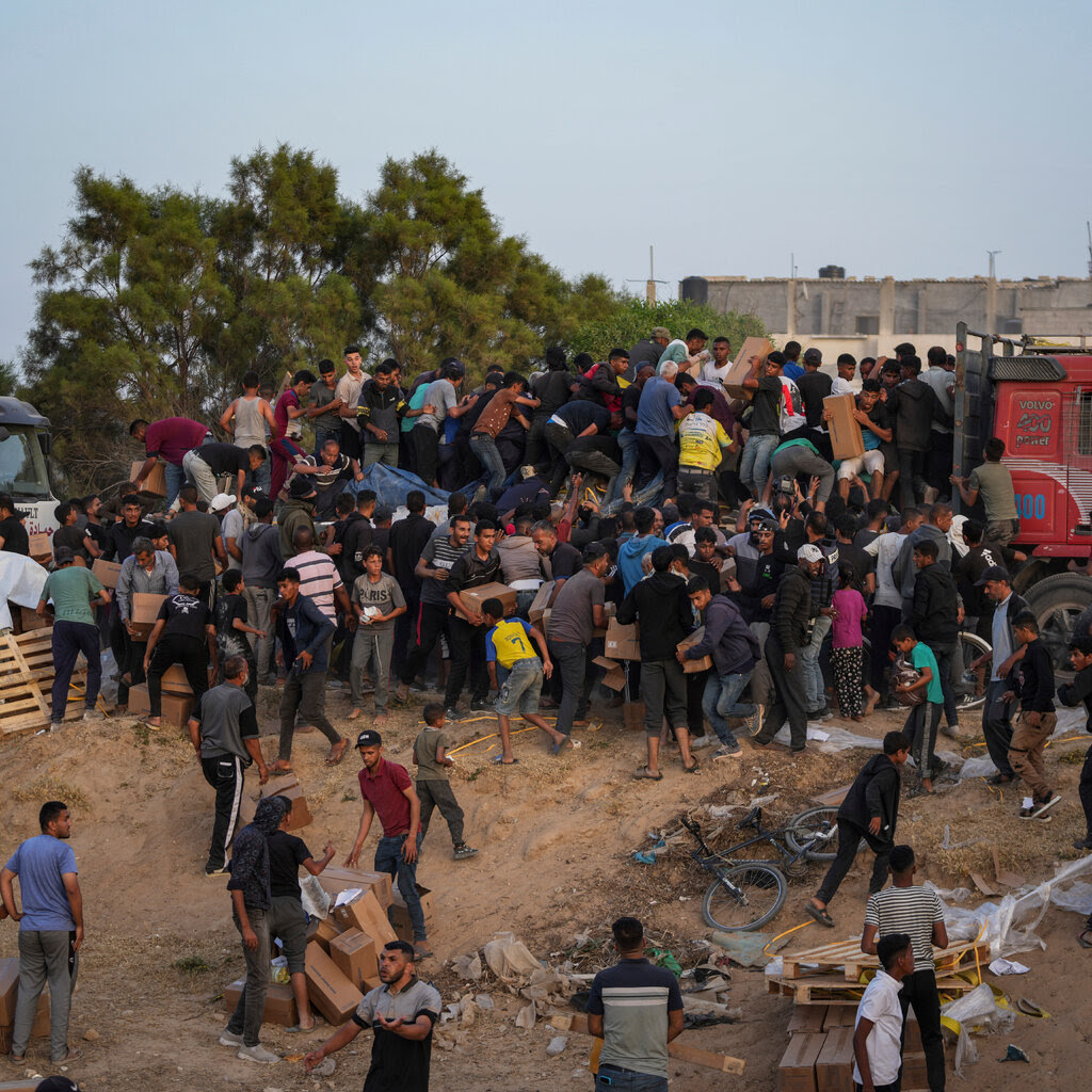 A crowd of people climbing on top of a truck stopped on a dusty hill. 