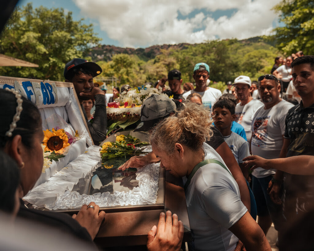 A woman crying over an open coffin as people stand nearby.