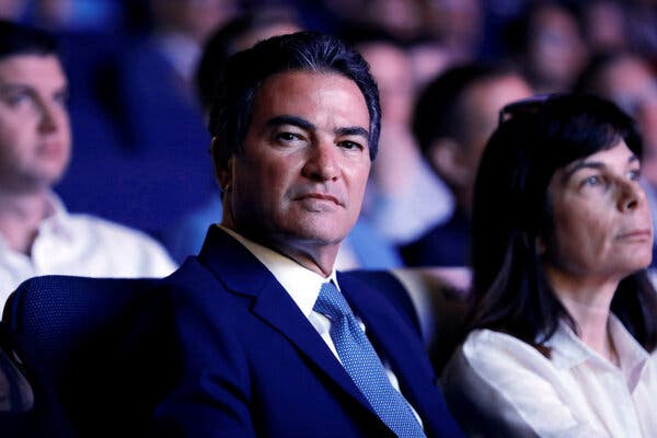Yossi Cohen wearing a dark blue suit and tie sits in a crowd.
