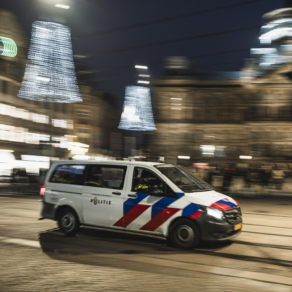 A white with red and blue markings drives along a city street.