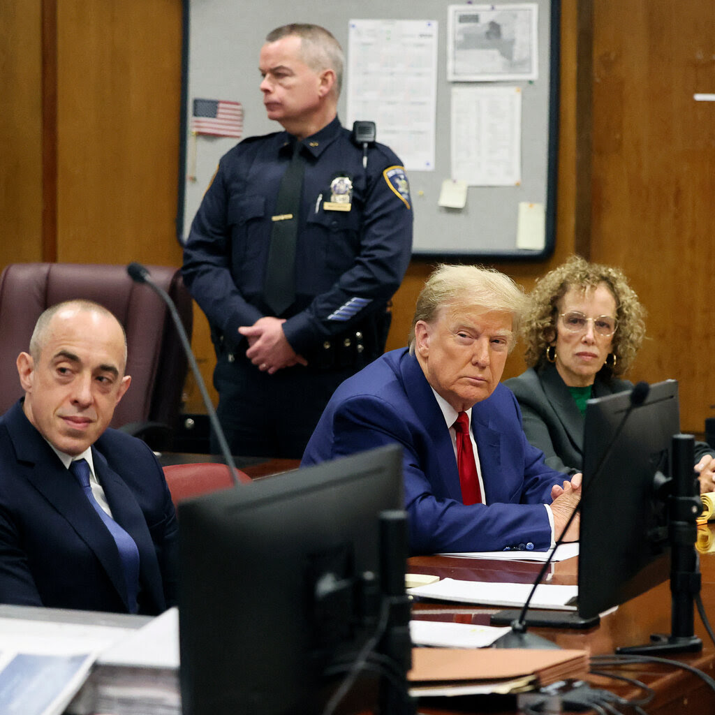 Donald Trump in a blue suit and red tie sits next to one of his attorneys at a trial hearing.