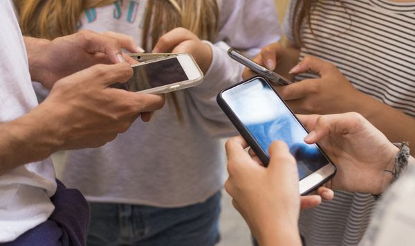 A group of young people with mobile phones on the street. File photo credit: carballo via Shutterstock.