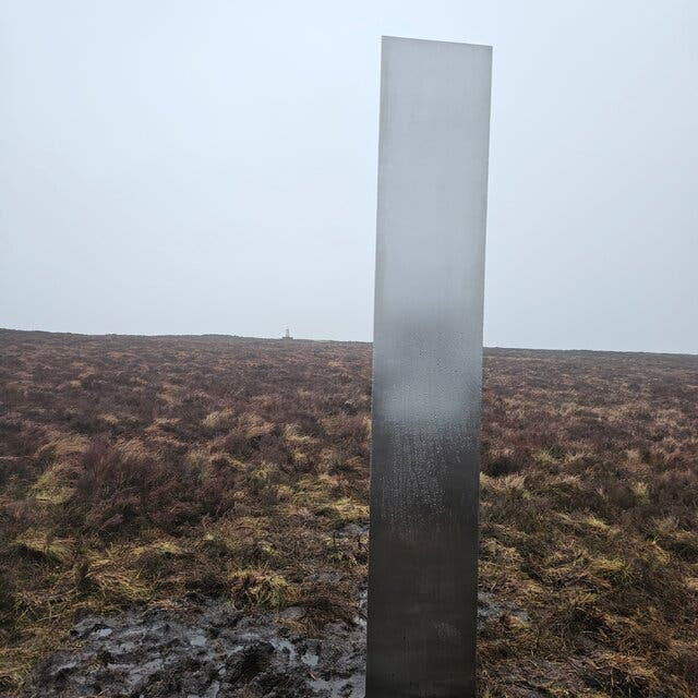 An upright slab of metal 10 feet tall stretches vertically from a brown landscape.