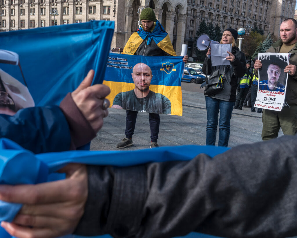 Demonstrators hold Ukrainian flags with people’s pictures on them in a public square.