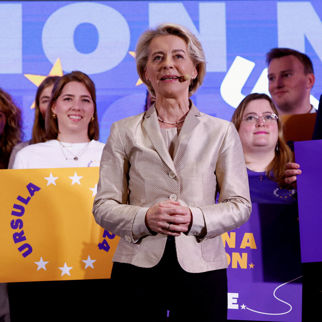 Ursula von der Leyen, president of the European People’s Party, speaks on a podium as she is flanked by young people carrying placards. 