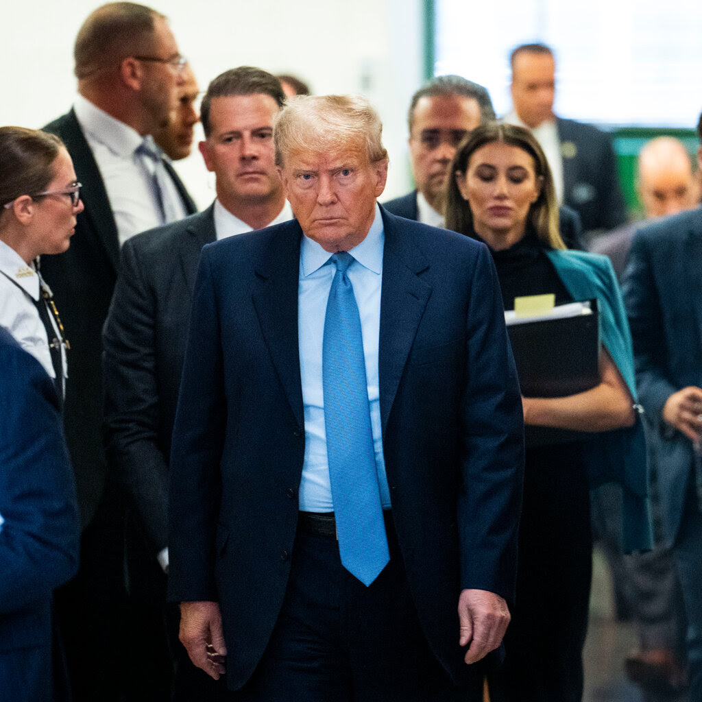 Donald Trump walking in a courthouse hall in a navy suit and blue tie.