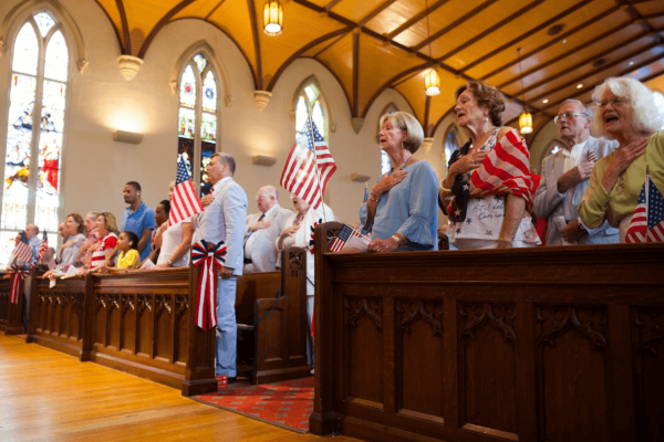 People sing in church filled with American flags. One woman is wrapped in an American flag.