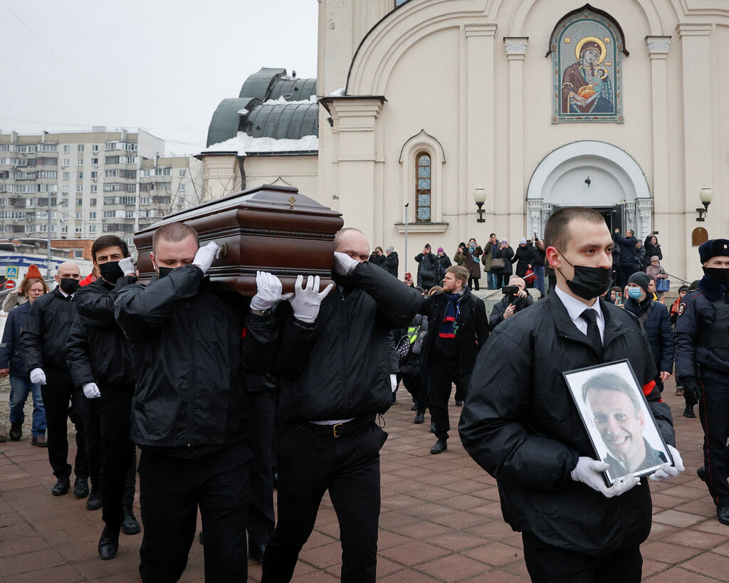 Funeral workers carrying a casket and a photograph of Navalny outside a church.