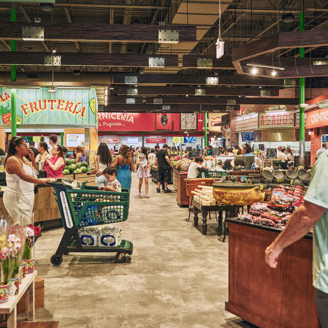 People push shopping carts through the aisles of a brightly lit grocery store.