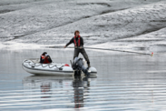 Researchera in Alaska collecting passive acoustic data on a small, white boat on calm waters. Snowy banks appear in the background.