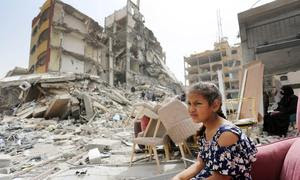 Una niña sentada entre los escombros de edificios destruidos en Gaza.