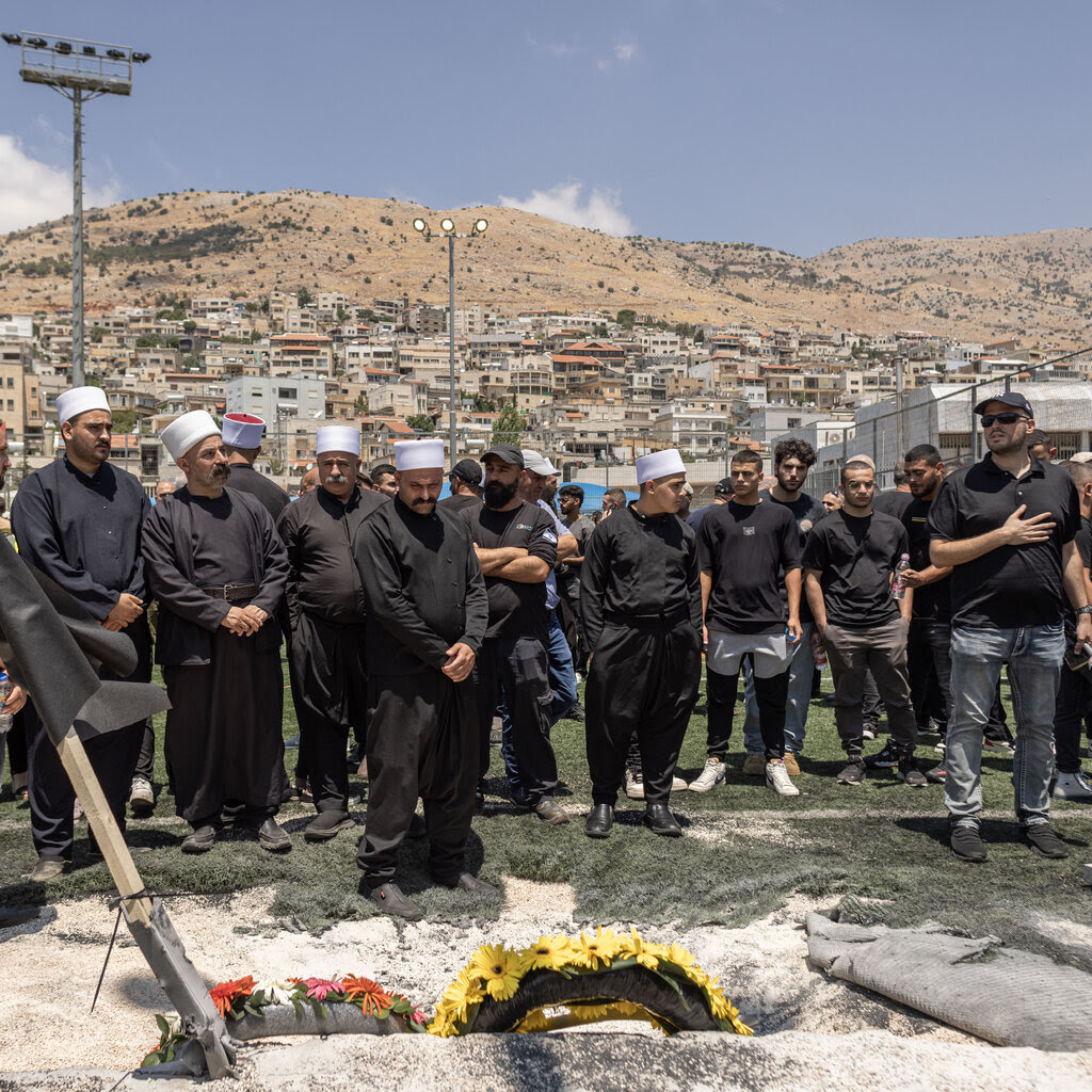 A group of men gathered on a soccer field with hills in the background.