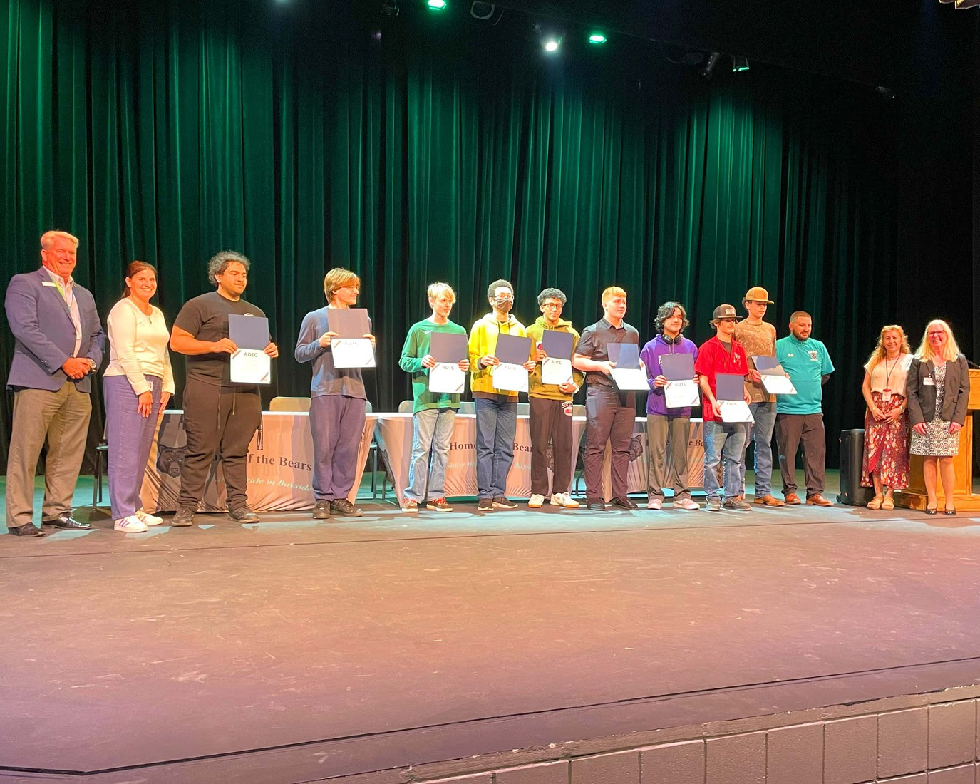 The group of graduates hold their diplomas and stand alongside BPS representatives