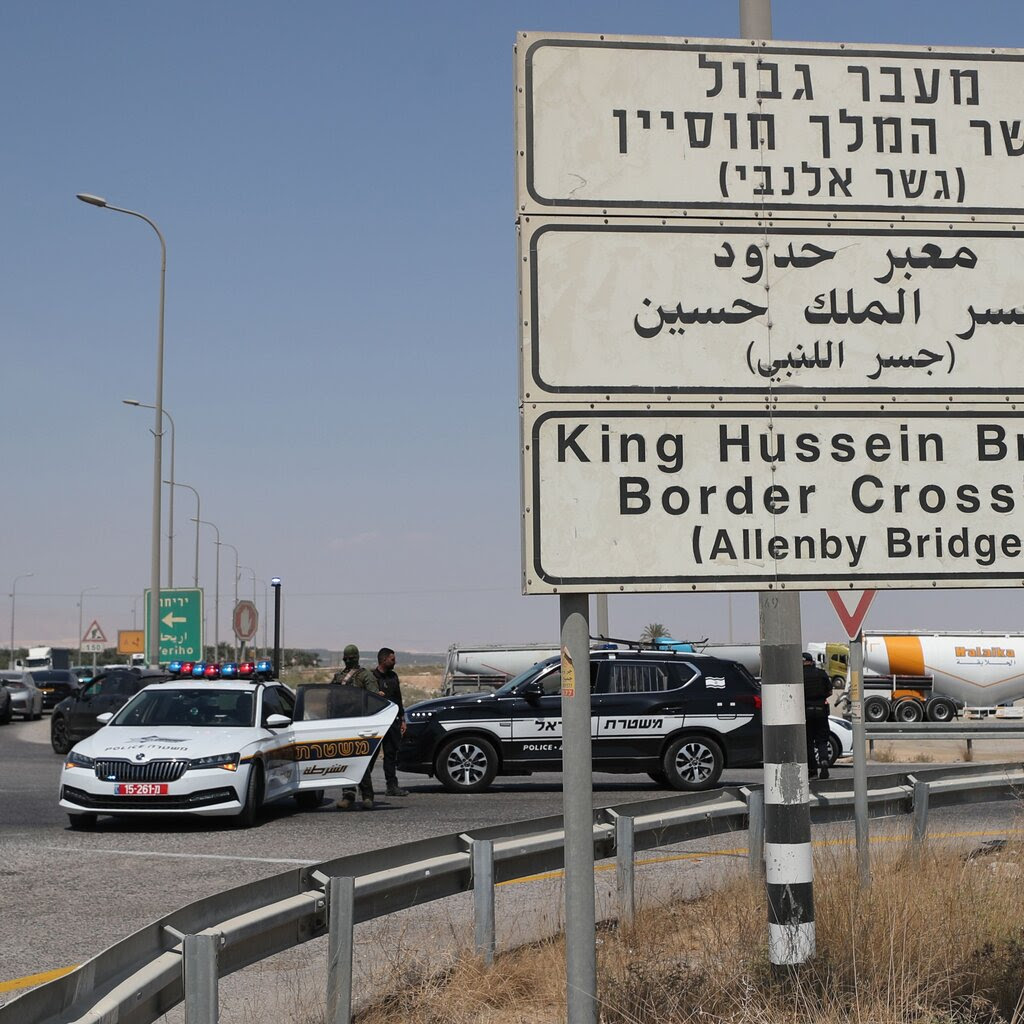 Several people stand near police vehicles behind a sign for the Allenby Bridge crossing.