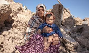 Una mujer sostiene a un niño de 6 meses sentada entre los escombros de las casas destruidas por un terremoto en Afganistán.