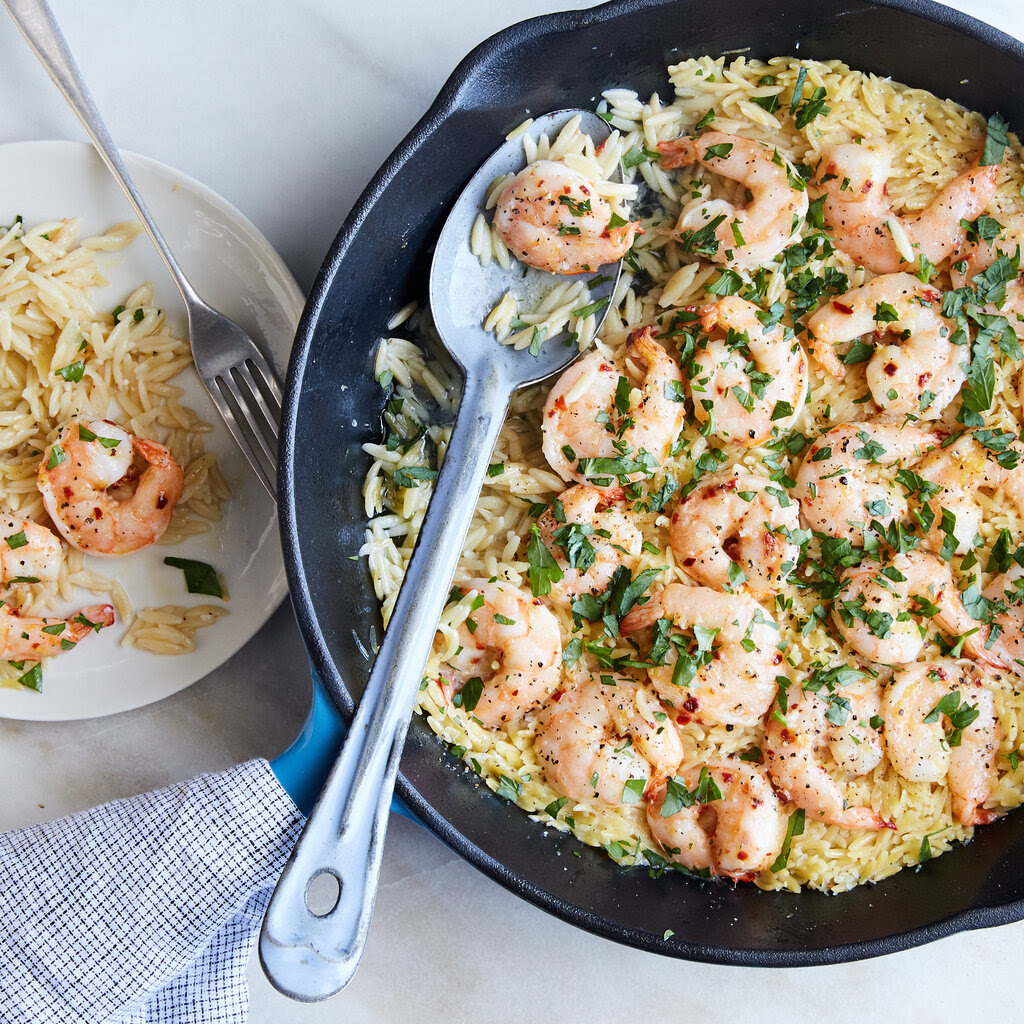 A blue skillet holds shrimp scampi with orzo and a serving spoon.