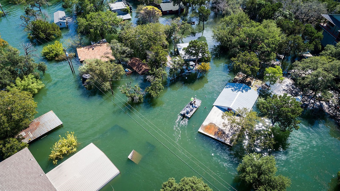 A boat navigates between houses in a flooded town (Credit: Getty Images)