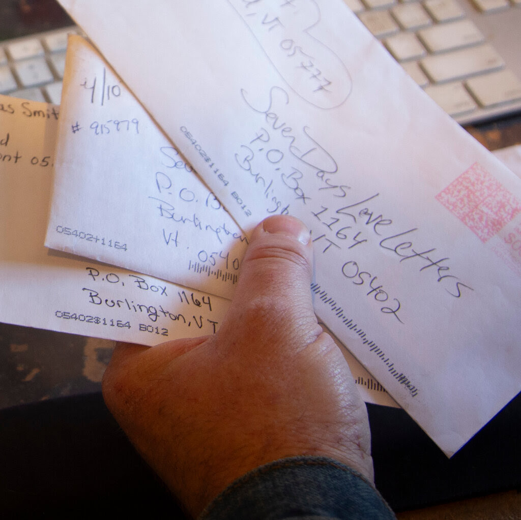 A hand grasps a few handwritten envelopes, with other papers scattered on a desk near a keyboard.