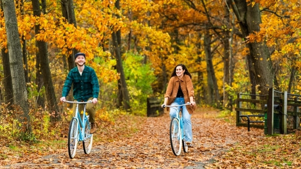 Man and woman riding bike on forest trail during the fall.