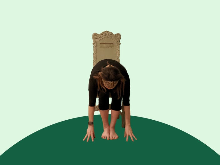 Woman doing chair yoga forward fold on green background.