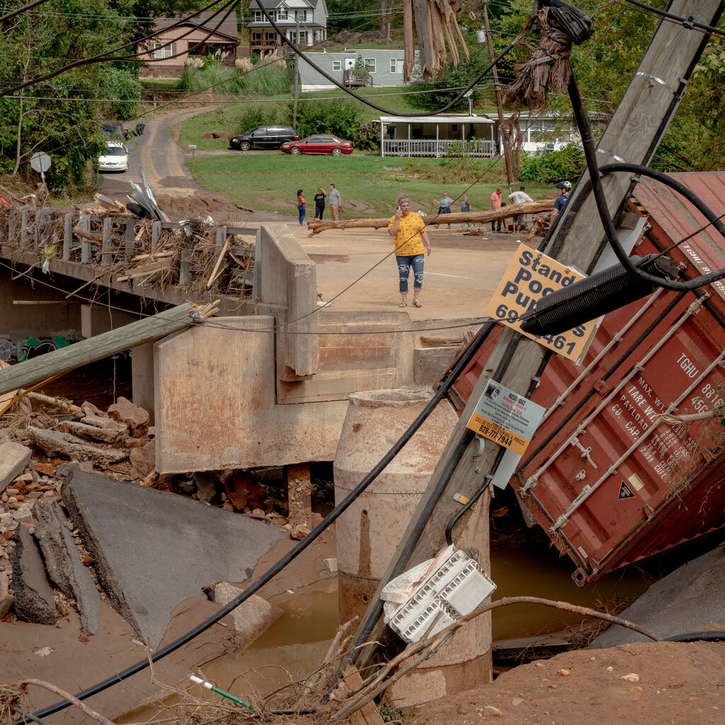 A person stands on a bridge among debris and a washed out road.