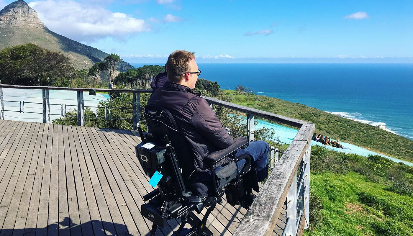 John seated in his wheelchair at a scenic overlook in South Africa.