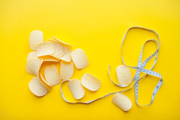 Chips and measuring tape on a bright yellow background weight loss and dieting concept