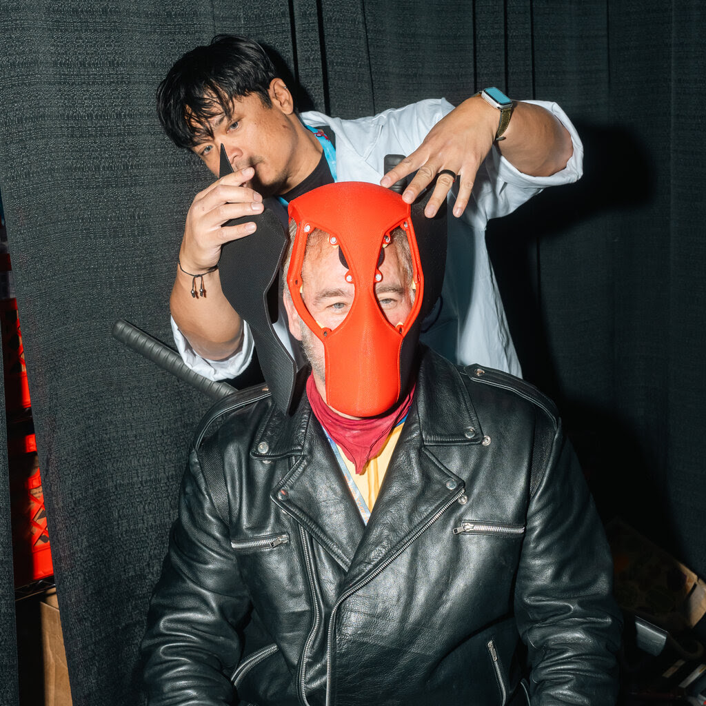 A man in a blue shirt examining a red mask worn by a cosplayer.