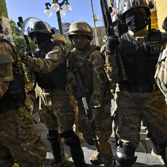 Soldiers carrying weapons and wearing helmets fitted with face shields.