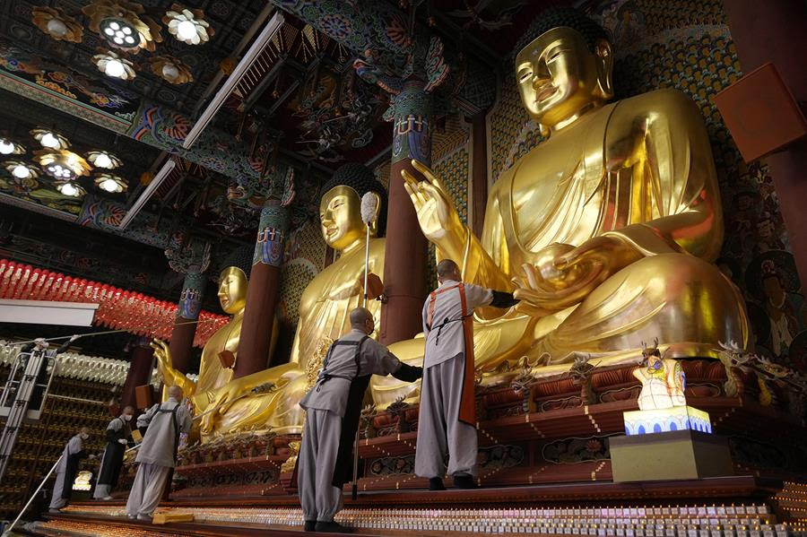 Buddhist monks clean large golden Buddha statues.