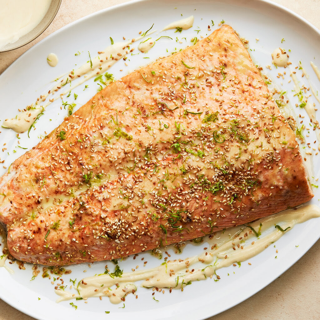 An oval platter topped with a large fillet of salmon scattered with scallions and sesame seeds with miso cream sauce is photographed from overhead. 