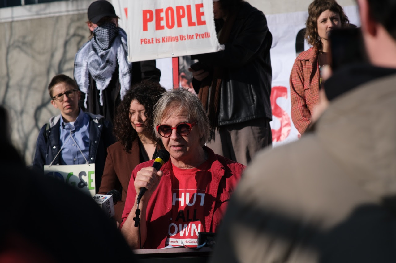 Picture of speaker at rally against rate hike and decision to
keep Aliso Canyon Gas Facility open indefinitely with a shirt that
says Shut It Down. Behind the head of the speaker is a sign that says
PG&E is Killing Us for Profit