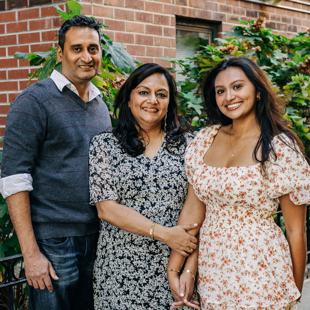 A portrait of Jay Krishnamoorthy, wearing a sweater, and Vidya Jayaraman and Rithika Jayaraman, both wearing floral dresses.