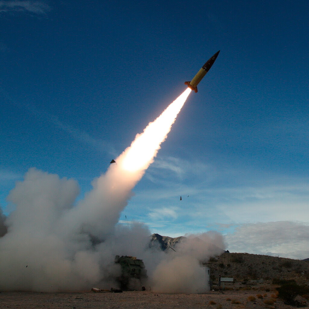 A missile is launched from the ground with a fiery trail across a blue sky.