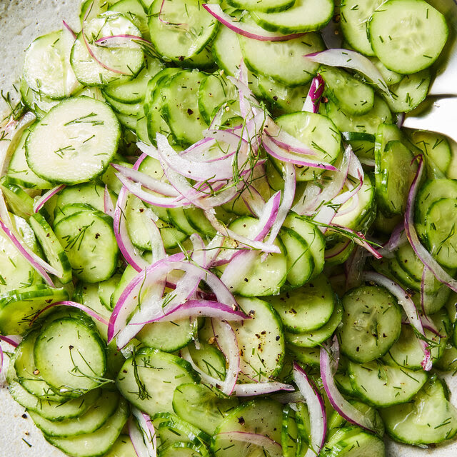 A salad with sliced cucumbers and onions on a white plate.