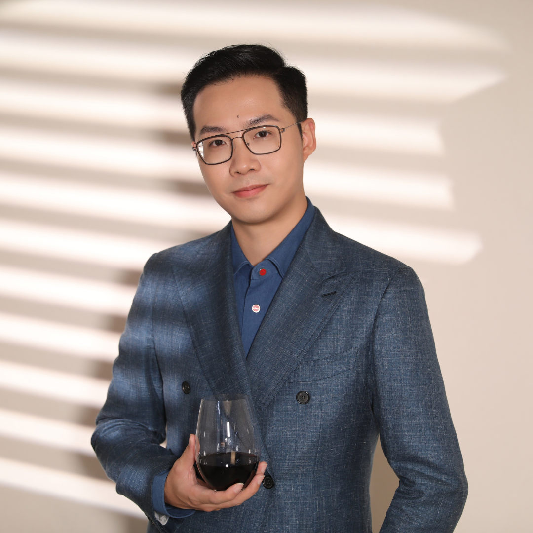 A person in a suit holding a glass of wineDescription automatically generated