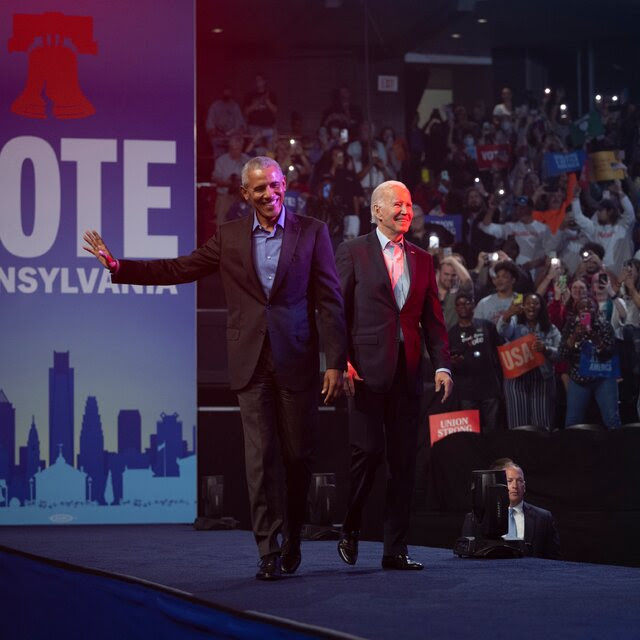 Former President Obama and President Biden smile at a crowd while on a stage with a sign that reads, “Vote Pennsylvania.”