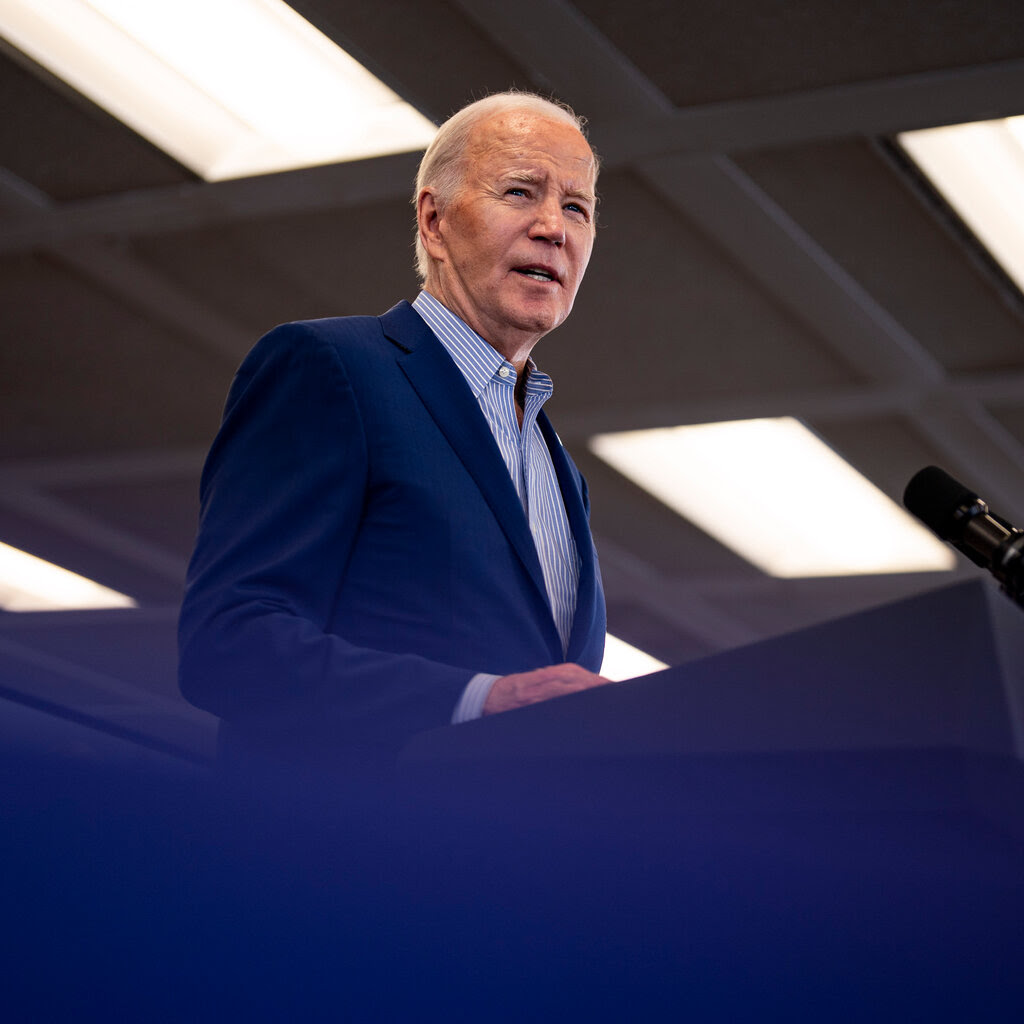 President Biden, in a blue jacket and shirt, standing at a lectern.