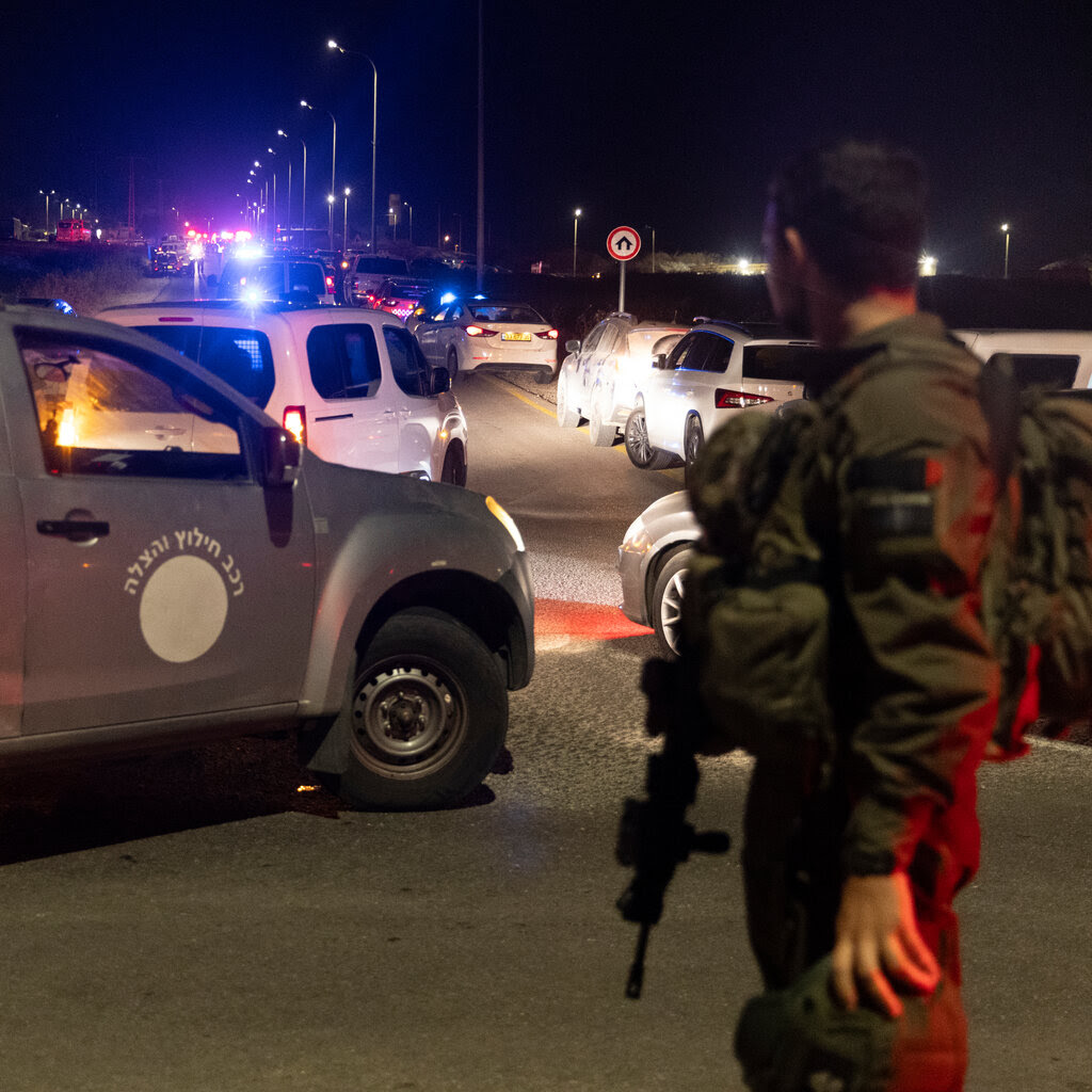 A soldier holding a rifle watches a road where cars are lined up at nighttime.