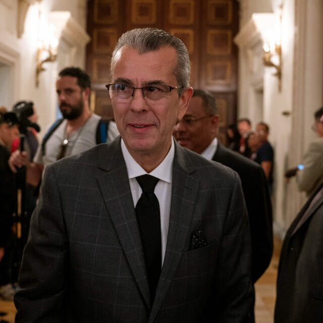 A man wearing a suit in a corridor full of people.