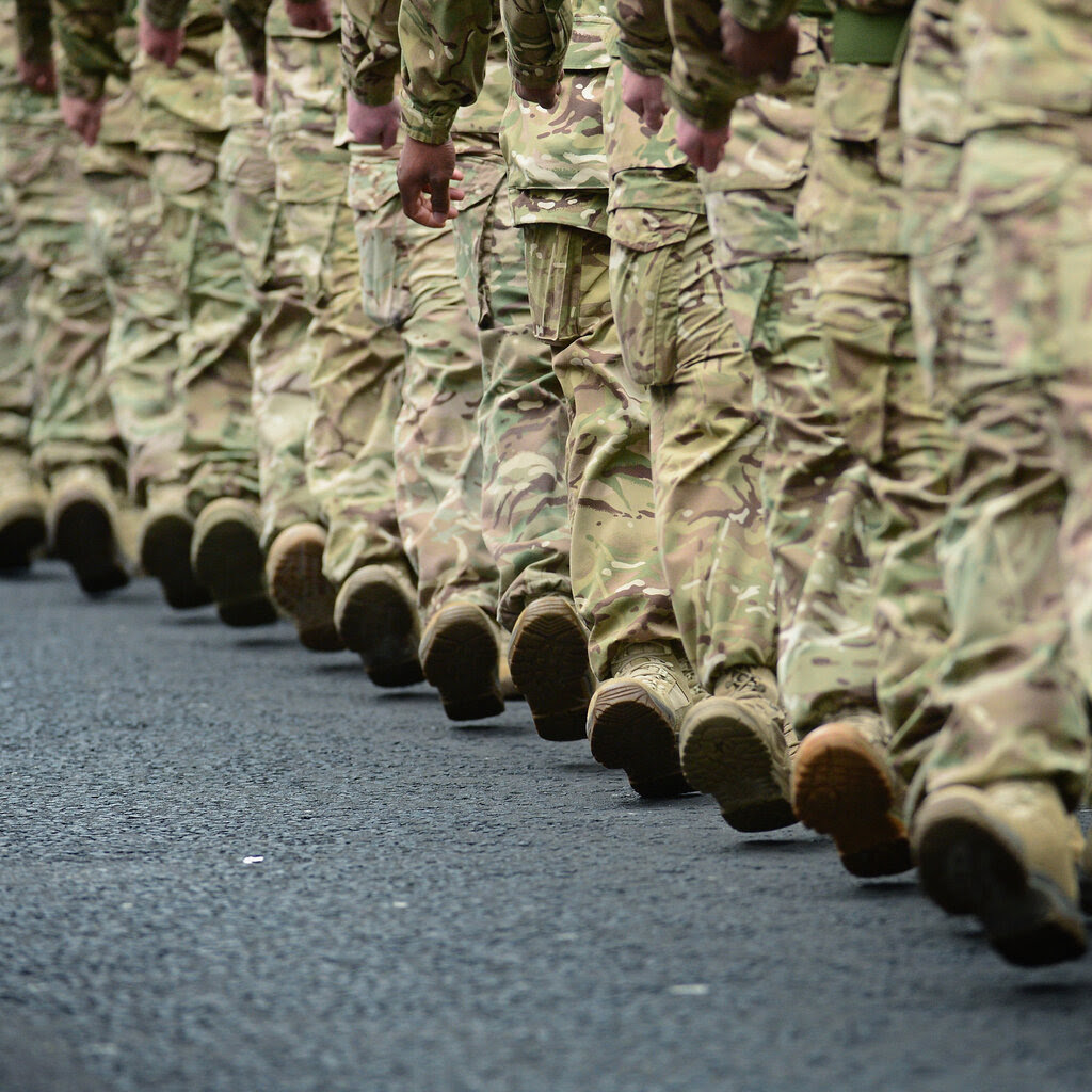 A group of soldiers marching in camouflage uniforms seen from the waist down.