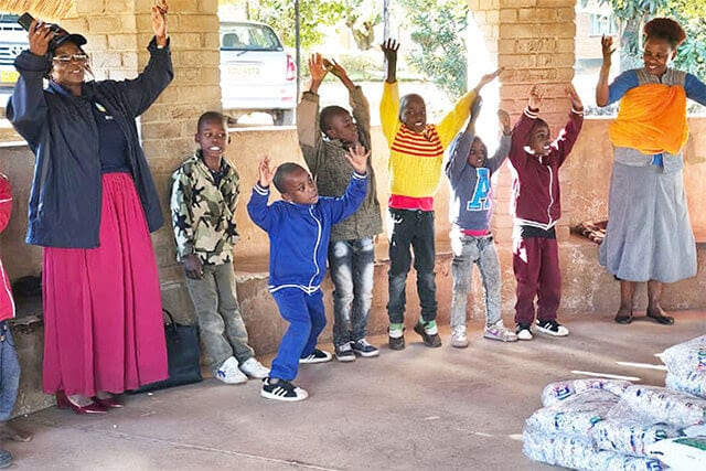 Florence Kachingwe (left, in pink skirt), chairperson of The Class of 81 Charitable Foundation, sings and dances with kids at Fairfield Children’s Home, a United Methodist-affiliated children’s home in Mutare, Zimbabwe. The foundation, started by former students at United Methodist Hartzell High School, donated food and other supplies to the school. Photo by Tafadzwa Gumbochuma.